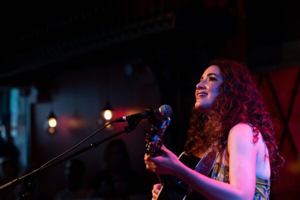 Color photo of a musician playing a guitar at a stand mic.