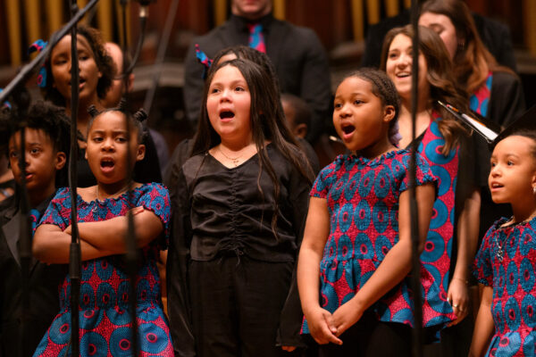 Color photo of a children's choir singing onstage.