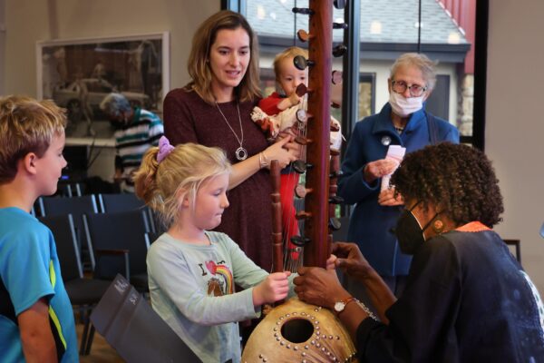 Color photo of a musician explaining her instrument to children and audience members.