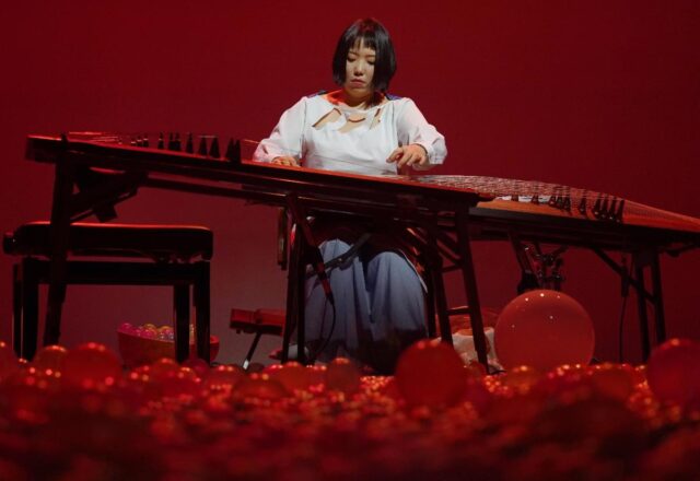 Musician Seo Jungmin is bathed in red light as she performs. Red balloons cover the floor.