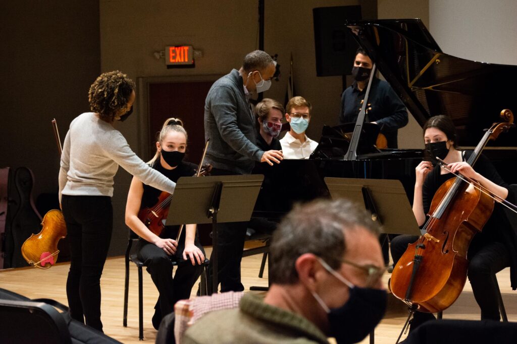 Color photo of masked musicians working with students in an orchestra master class.