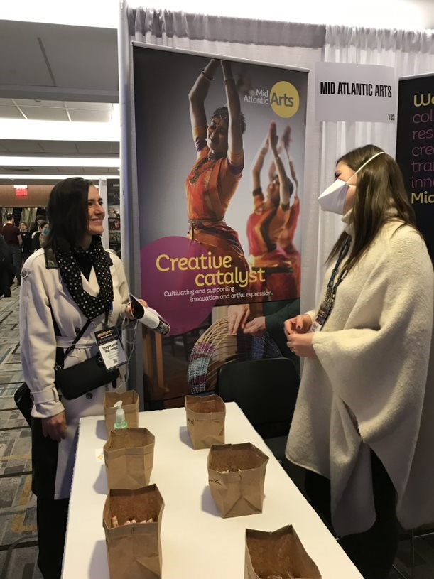 Color photo of two people speaking at a conference booth.