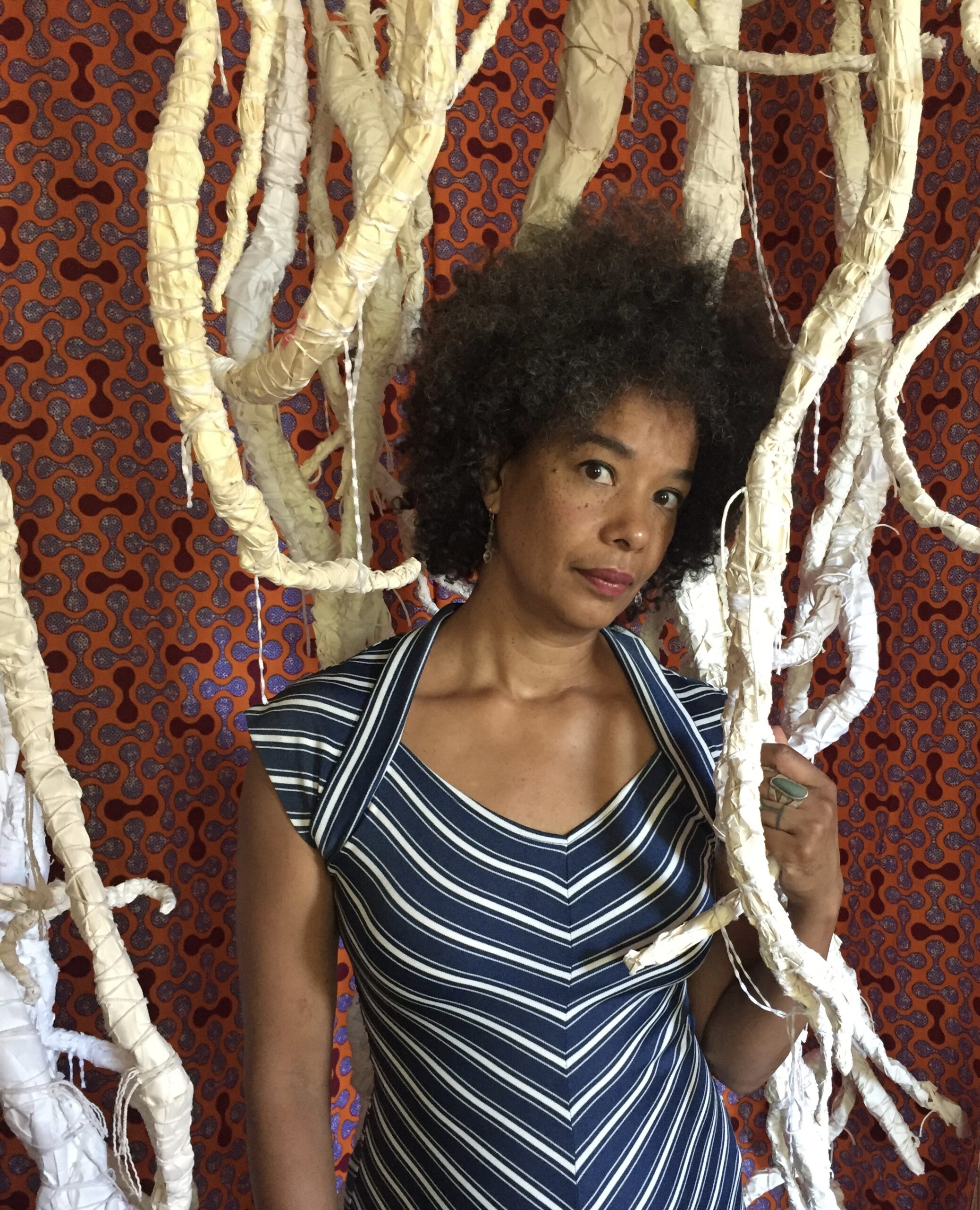 Color photo of Edisa Weeks standing among artistic roots hanging from the ceiling.