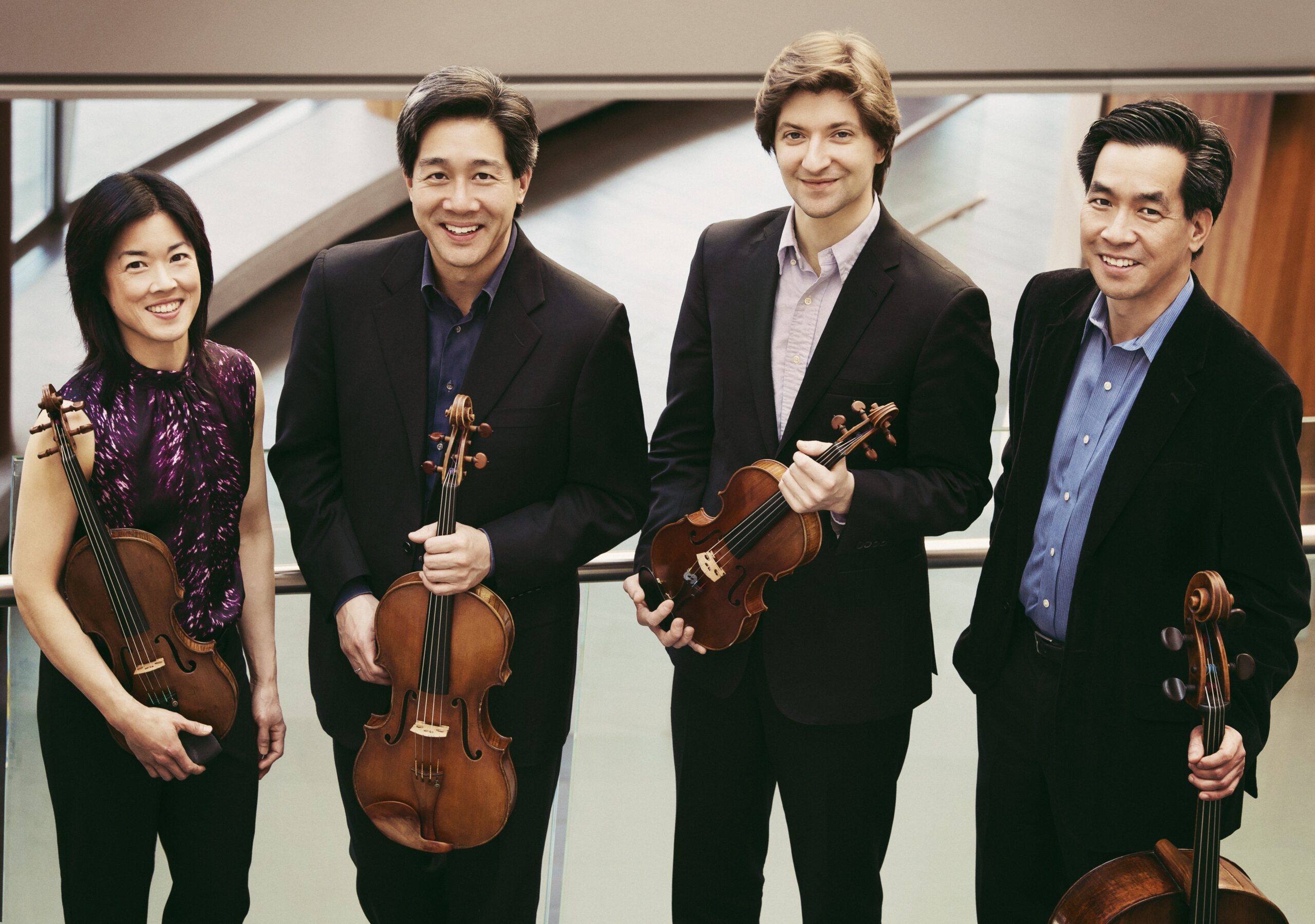 Color photo of four musicians posing with their stringed instruments.
