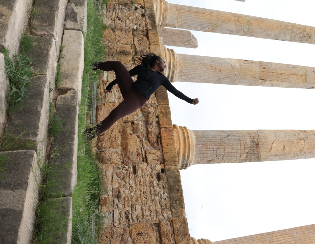 A lone dancer poses outside at the top of ancient stone steps framed by stone columns.