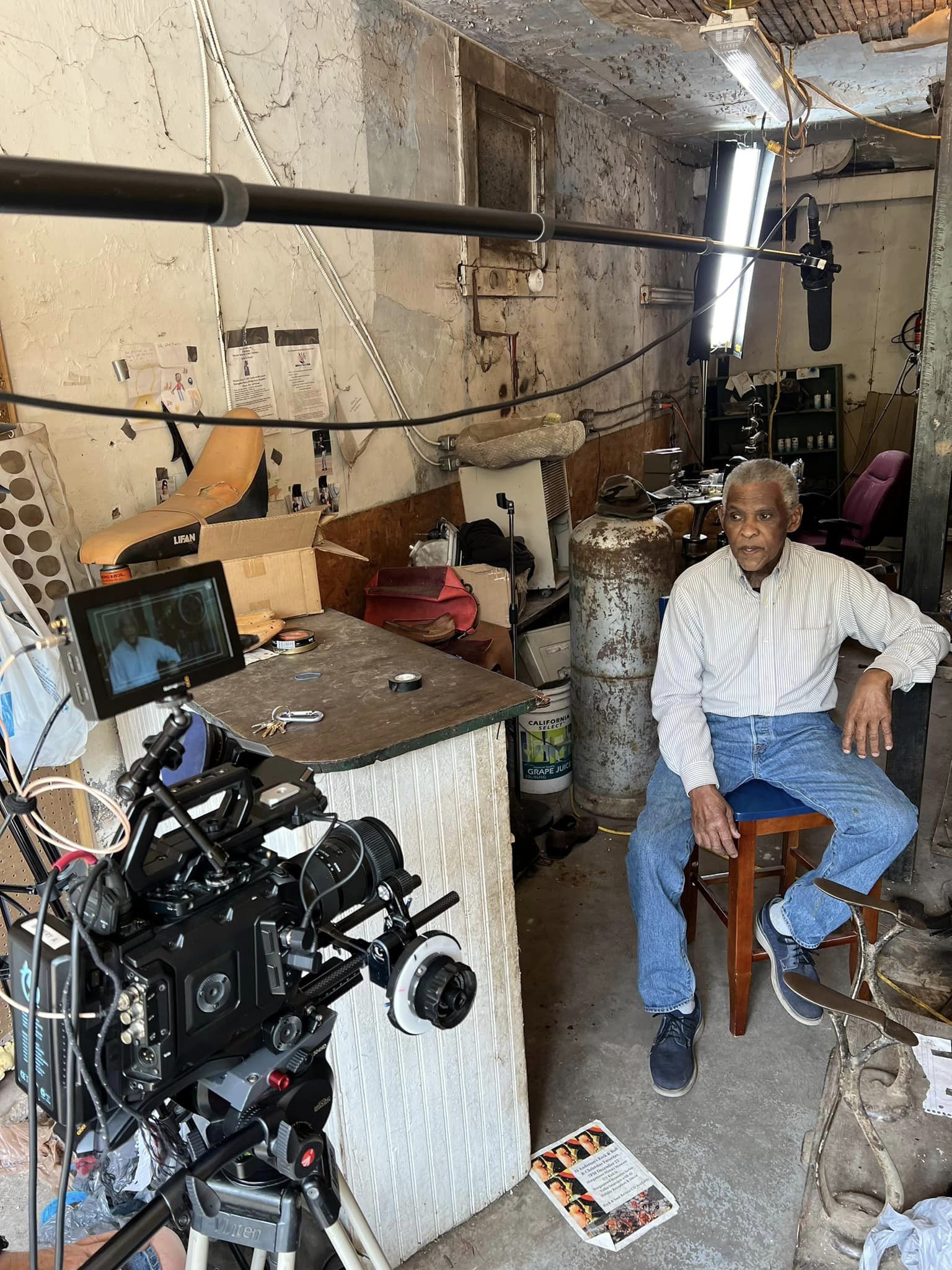 A man sits in a concrete room with a camera and laptop recording equipment in front of him.