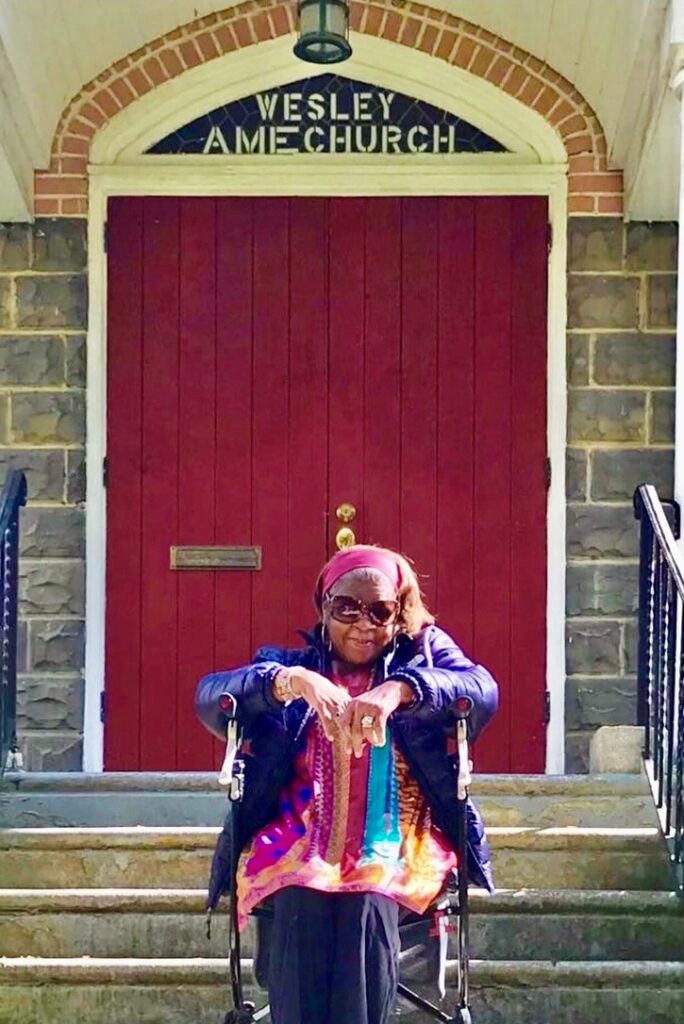 Color photo of a woman in a wheelchair outside of a large red church door.