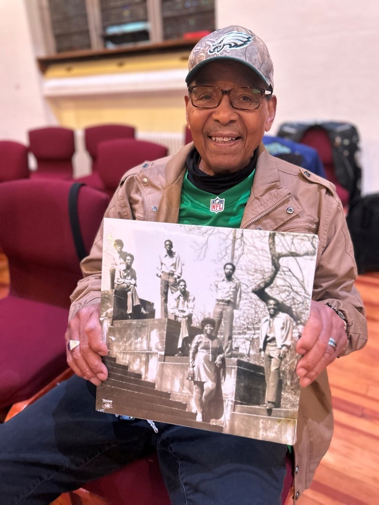 Color photo of a seated man holding a record album cover.