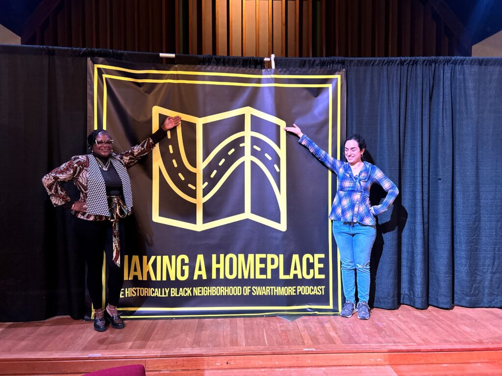 Color photo of two women stand on a stage on either side of a Making a Homeplace banner.