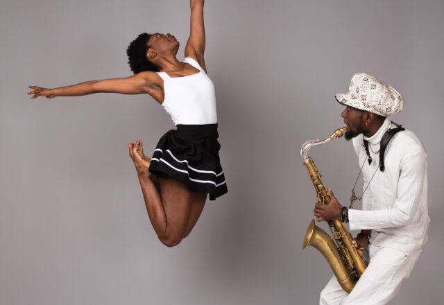 Color photo of a dancer leaping on the left while a man plays a saxophone on the right.