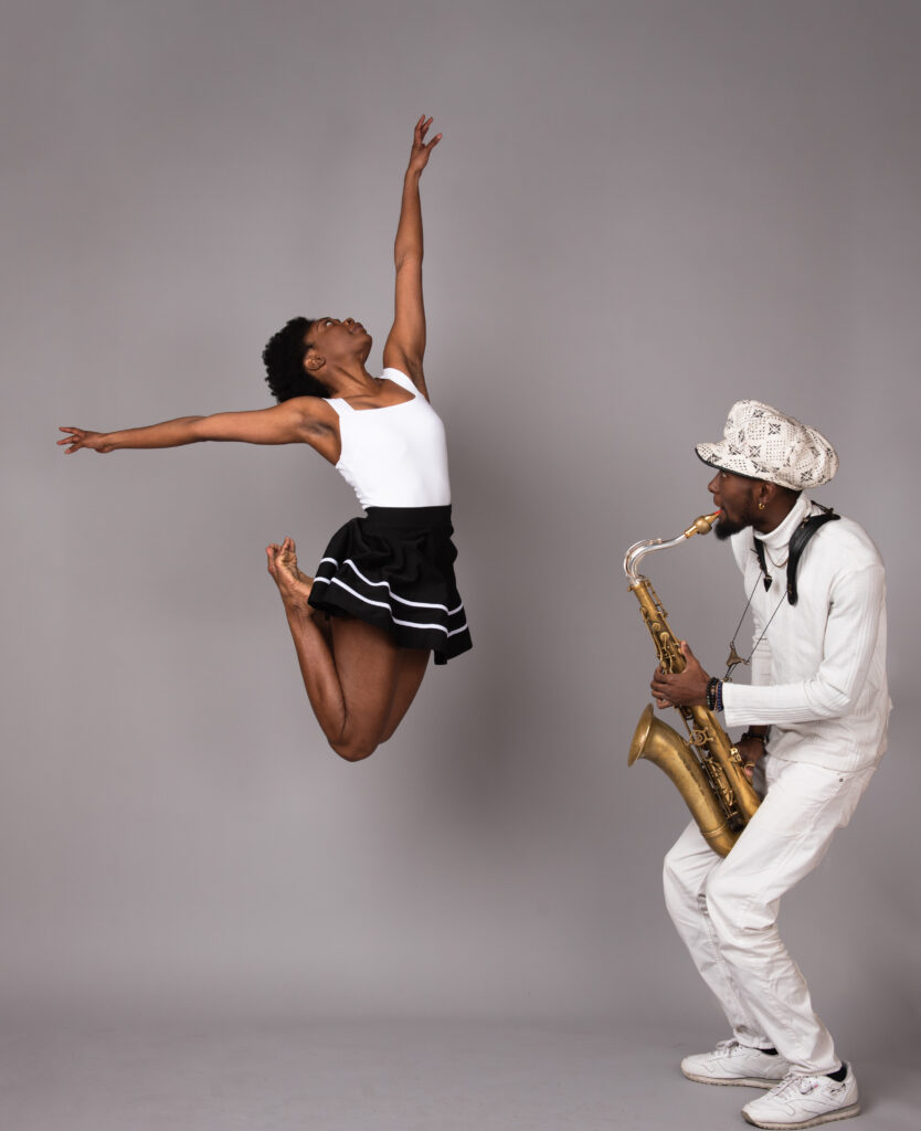 Color photo of a dancer leaping on the left while a man plays a saxophone on the right.