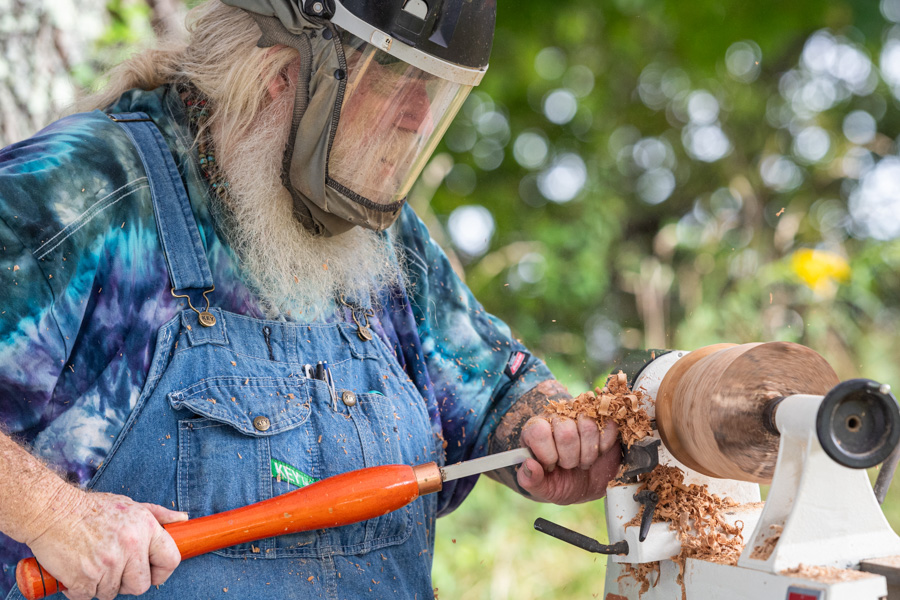 I man stands outside and turns wood using a chisel and lathe.