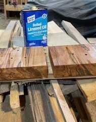 Slabs of wood dry while a can of linseed oil is visible behind them.