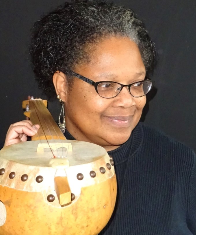 Dr. Dena Jennings headshot. She holds a traditional African stringed instrument.
