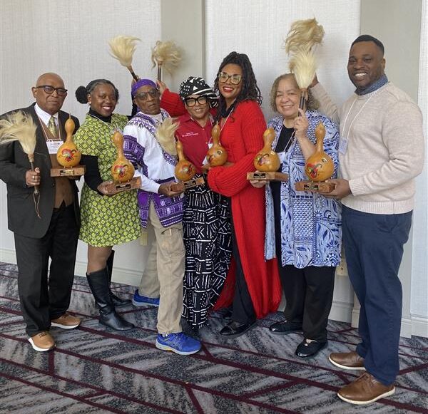 A group of people hold gourd awards and cow tail switches while smiling for the camera.