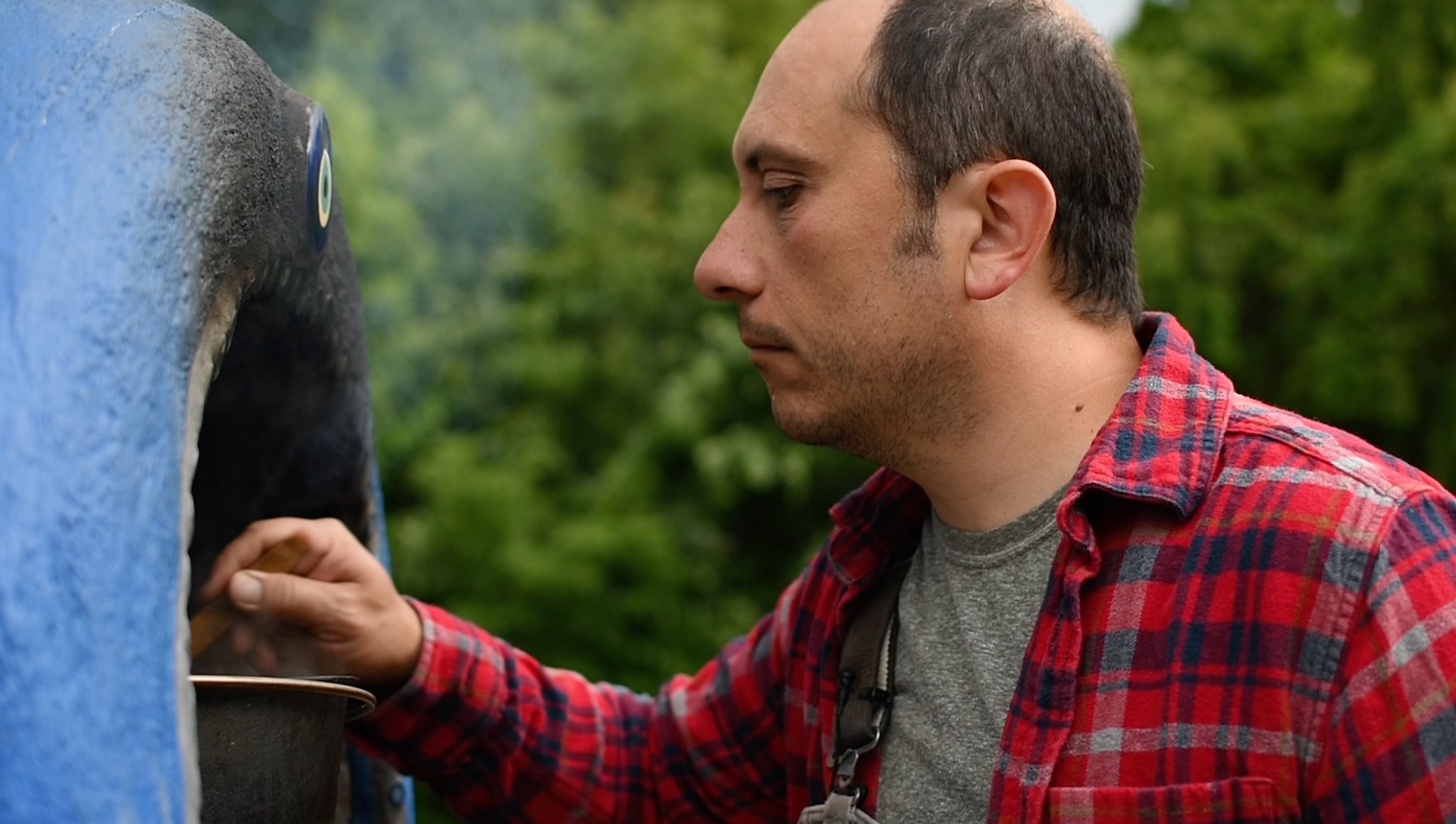 Mehmet Öztan stands outside and is reaching into a smoking oven.