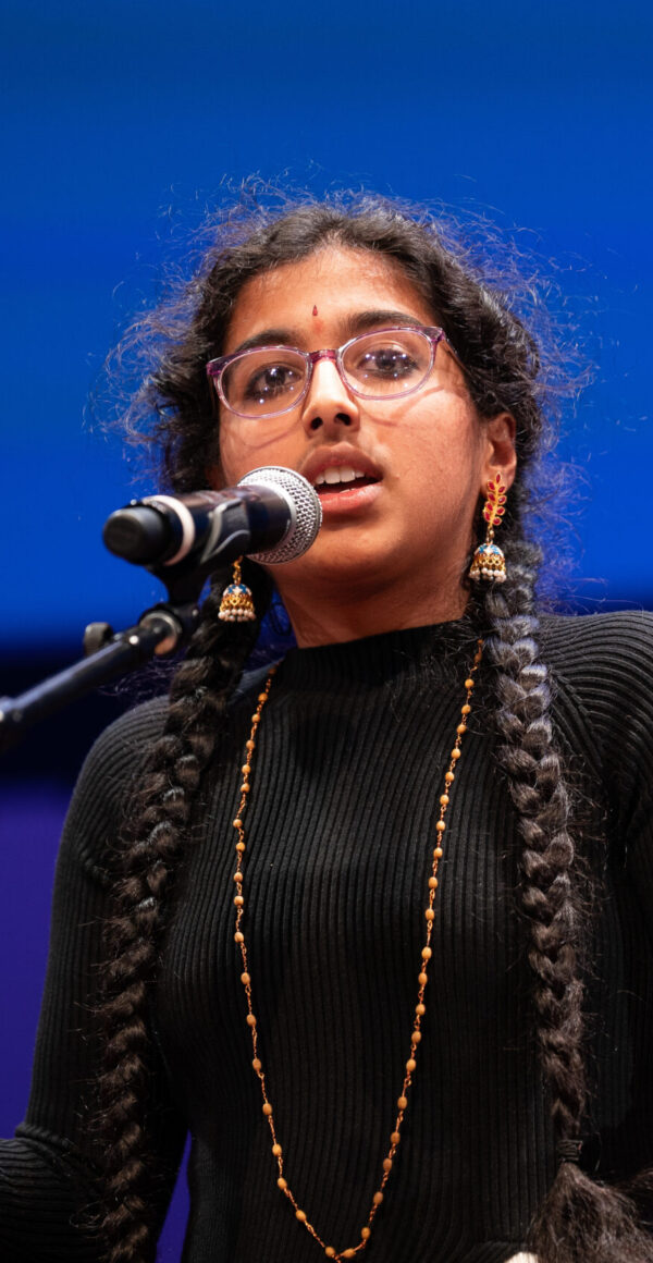A young woman stands at a mic on stage. She is reciting.
