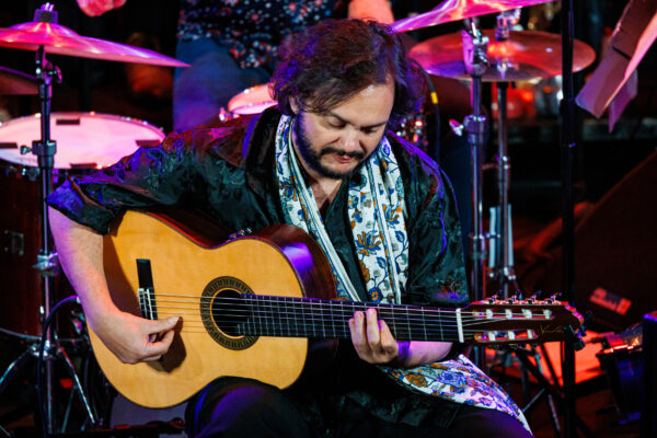 A musician sits on a stage playing and acoustic guitar.