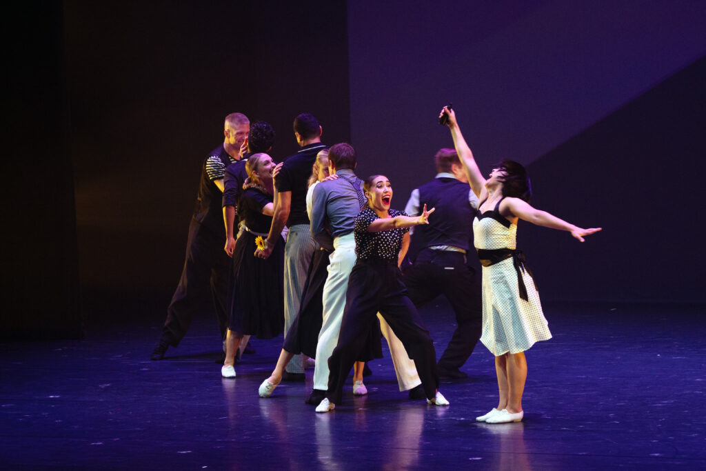 A group of nine dancers stand in a line in a variety of active poses.