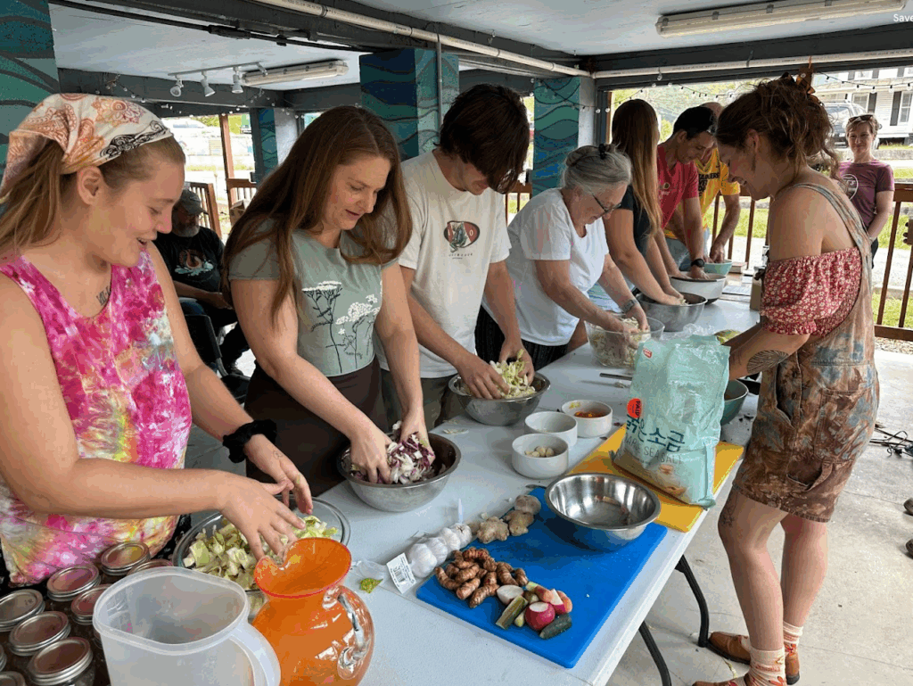A group of people stand at long tables doing food prep in bowls.