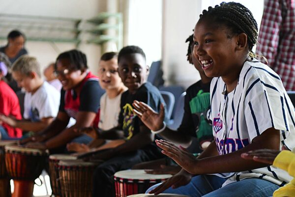 Excited students smile while playing African drums.