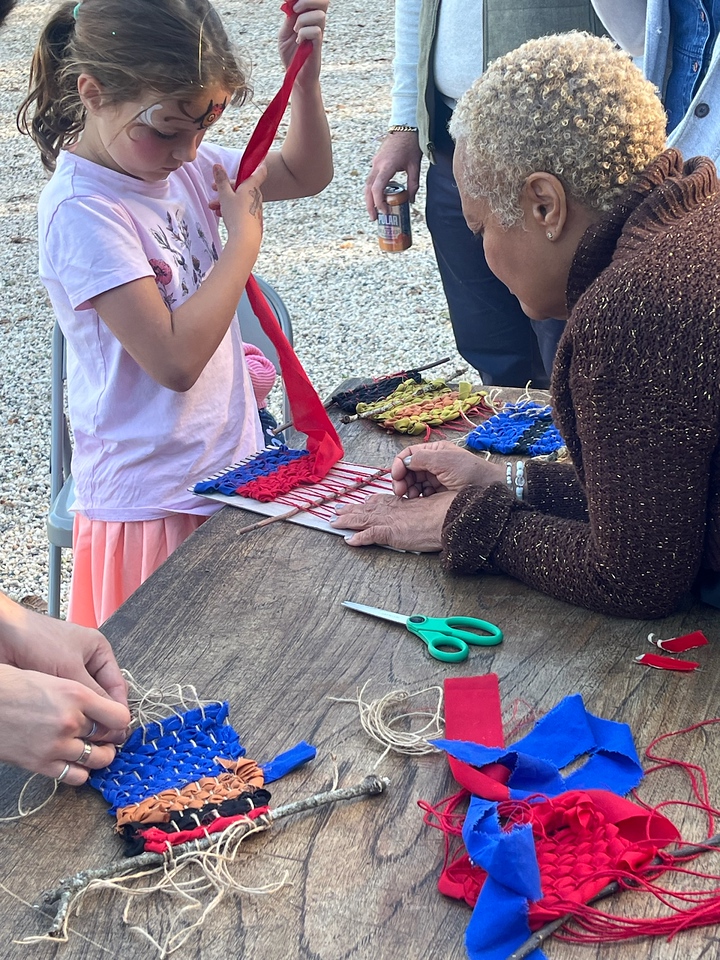 A young person works on weaving fabric while and older person walks them through the process.