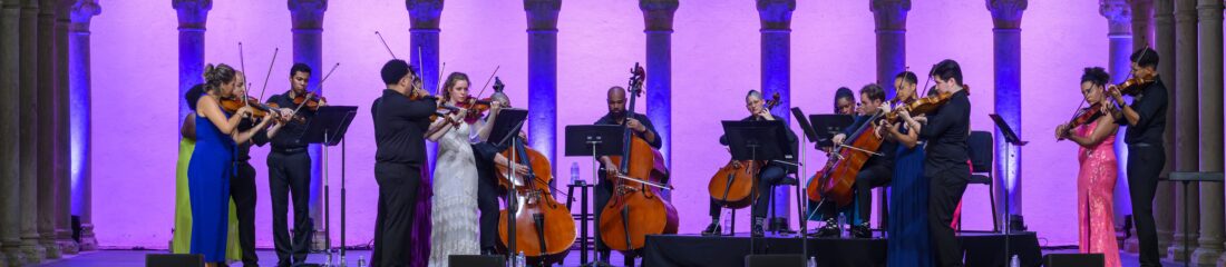 A group of musicians performs on a pink and purple lit stage.