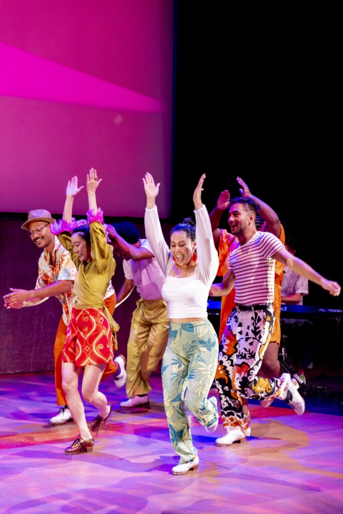 A group of brightly dressed dancers move joyfully across the stage.