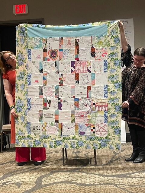 Two people holed up the finished quilt.