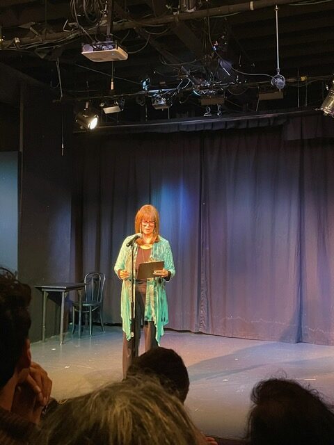 Valerie Vaughn stands on a stage and refers to a notepad in her hand while speaking into a microphone.