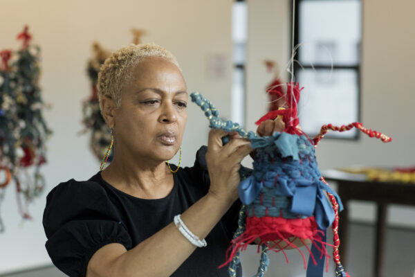 A woman works on a brightly colored mixed media object in a studio.