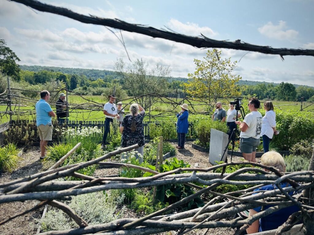 A group of people stand outside in a garden for a talk.