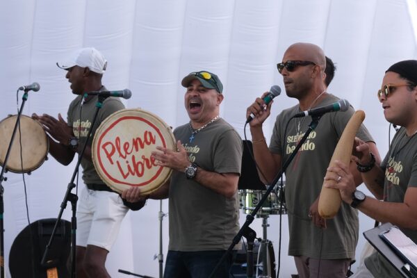 A group of musicians sing and play traditional images on an outdoor stage.