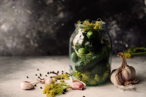 A jar of pickles with dill, garlic, and peppercorns.