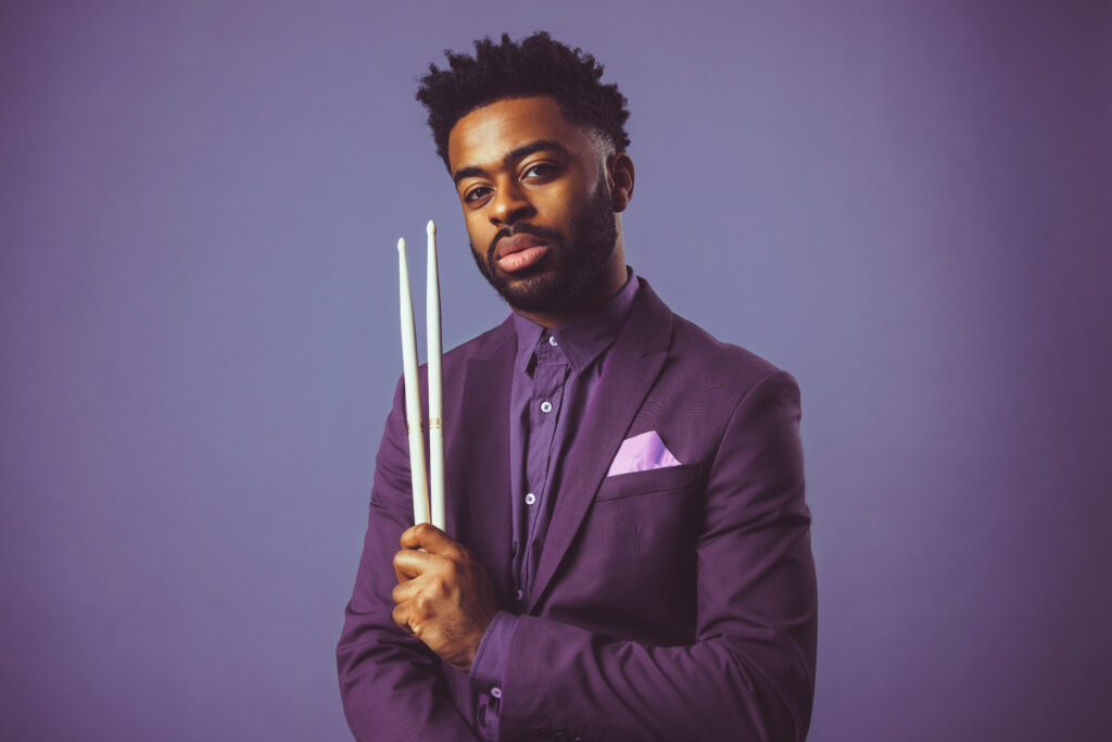 Jonathan Barber faces the camera holding drumsticks in his left hand.