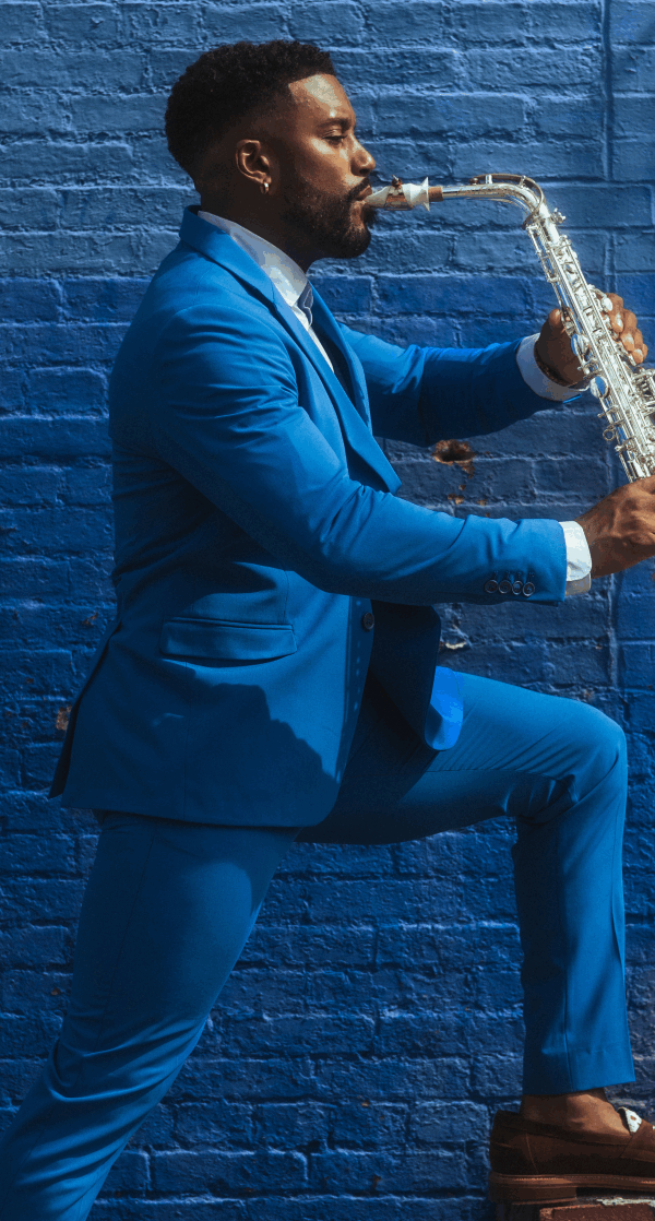 Brent Birckhead posing to the right with his leg propped up playing the Alto Saxophone