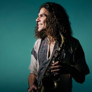 Antonio is posed against a teal green background and holds a saxophone.