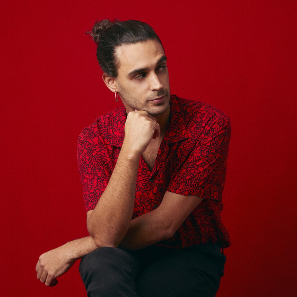 Pedro Pastor is posed seated against a red background.