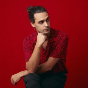 Pedro Pastor is posed seated against a red background.