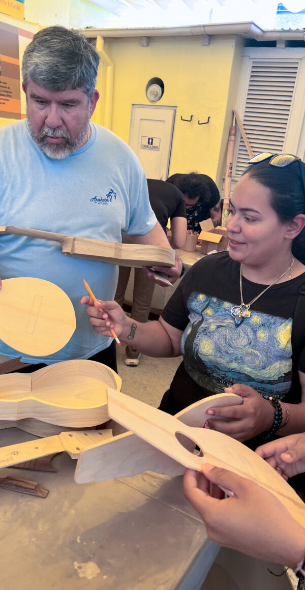 People work on crafting a small wooden stringed instrument in a workshop.