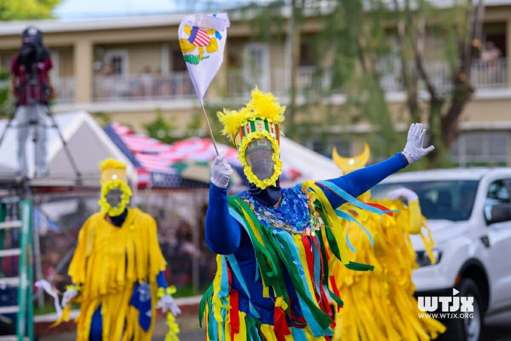 A parade with colorful dancers in costumes covered with ribbons wearing masks that obscure their faces.