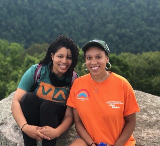 Siara Benoit and Takia Gaylord sit on a rock high above an old growth forest.