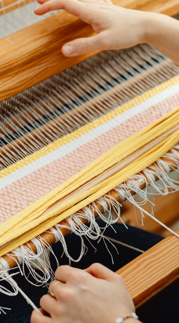 An artist uses a large loom to weave a rag rug.