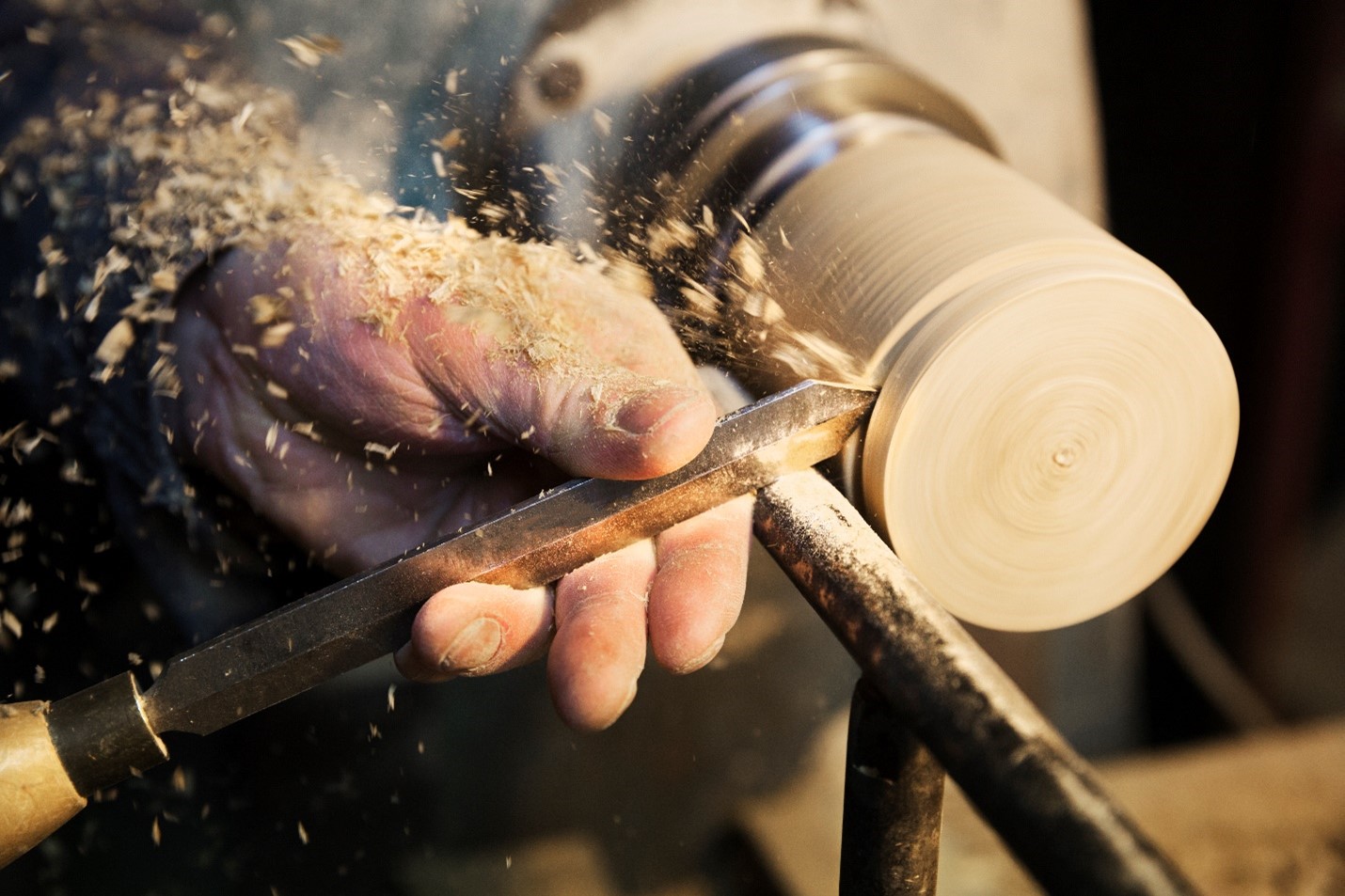 Close up of hands using a chisel while working a lathe.
