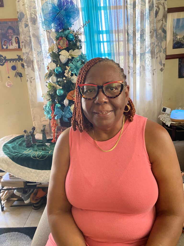 A woman sits in her home with a brightly decorated Christmas tree behind her.