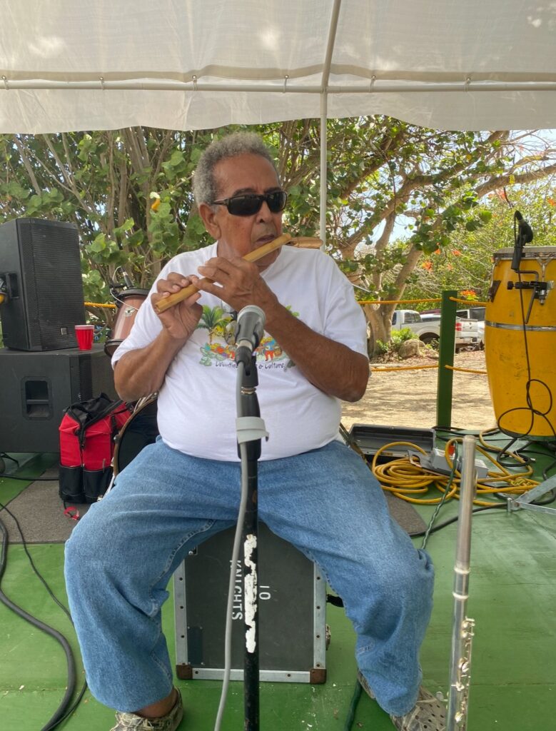 A man plays a wooden flute on a tented outdoor stage.