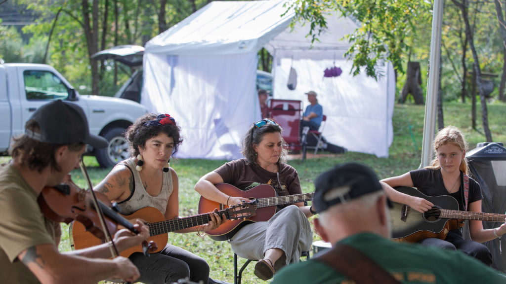 A group of people play stringed instruments at an outside festival workshop.