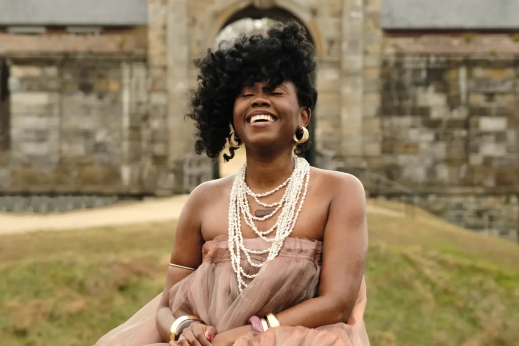 Ekep is posed outside in front of a medieval stone wall.