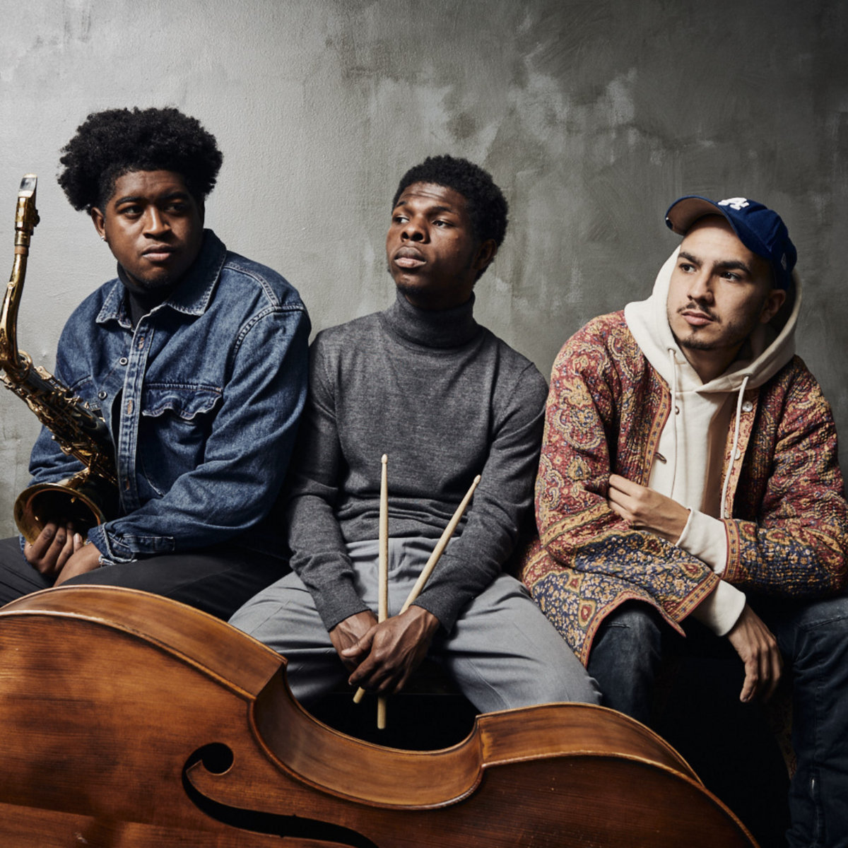 Three musicians hold their instruments and pose in a studio.
