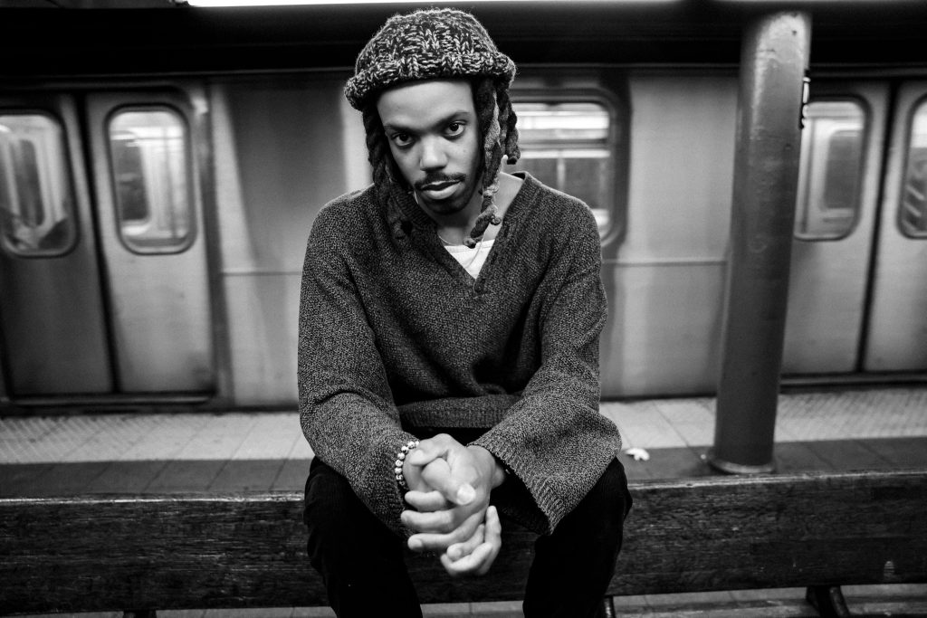 A man sits on a bench on a subway platform with a train behind him.